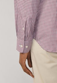 Camicia a maniche lunghe a quadri rossi e bianchi con polsini abbottonati. Presenta un colletto sottile e un orlo leggermente curvo. Tessuto in cotone testurizzato.