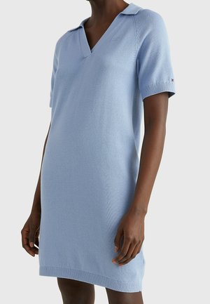 Gros plan d'une personne portant une robe tricotée bleu clair à manches courtes avec un col en V et un petit col.
