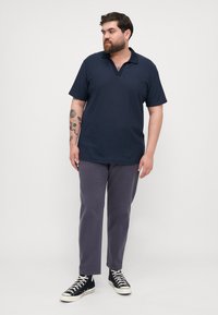 Navy short-sleeve polo shirt with striped texture, featuring a V-neck and collar; paired with gray trousers and black sneakers.