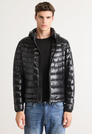 Black puffer jacket with hood, shiny material, horizontal quilted design, front zipper, and elastic cuffs. Worn over a black top and blue jeans.