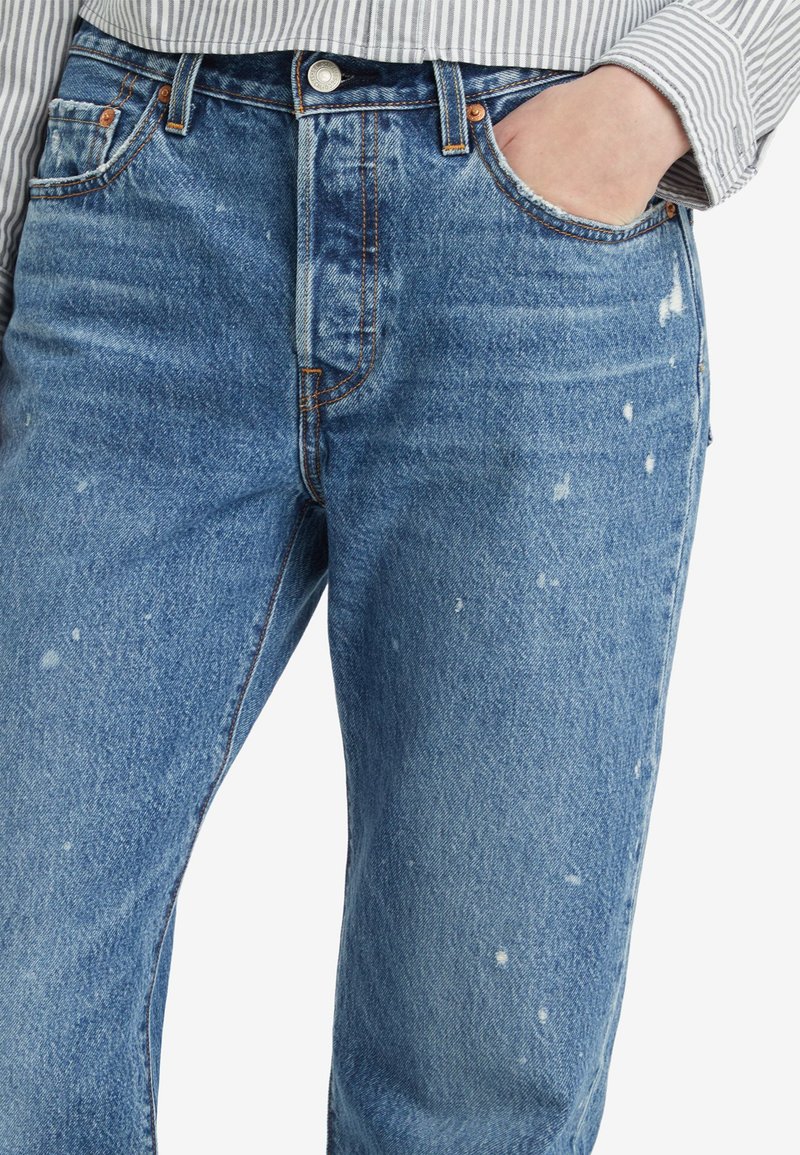 Jeans in denim blu con una finitura sbiadita, con whiskering visibile e lievi segni di usura. Design standard a cinque tasche con cuciture a contrasto.