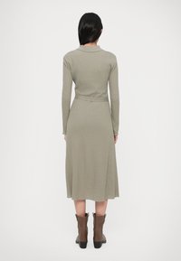 Langærmet, ribbet kjole i olivengrøn, indsnøret i taljen med bælte. Kjolens kant går til knæet og matches med brune ankelstøvler.