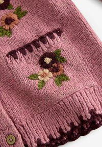 Puno neule vaaleanpunaisena tumman violetilla korostuksilla. Sisältää kukkakirjontaa kerma-, vaaleanpunaisen ja vihreän sävyissä. Mukana on taskuyksityiskohta.