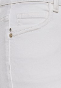 Jeans de mezclilla blanca con un bolsillo frontal, detalles de hardware en dorado y plateado, y una superficie lisa y texturada.