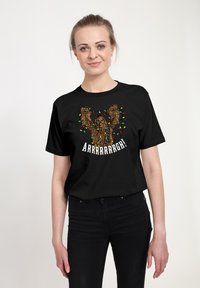 T-shirt en coton noir avec un graphique coloré d'une créature entourée de lumières de Noël et le texte "Arrrrrrrgh !" en blanc.
