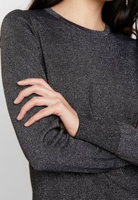 Grå långärmad tröja med metalltråd. Rund halsringning och snug passform, som visar upp en jämn textur och subtil lyster.