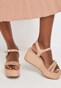 Nude platform sandalen met enkelbandjes, voorzien van kettingaccenten op de bandjes en een gladde leren textuur. Hoge wiggenhak.