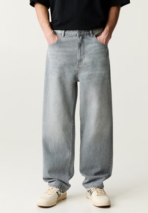 Light grey wide-leg jeans with a faded wash, featuring a button and zipper closure, and front pockets. Paired with beige sneakers.