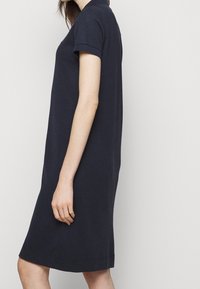 Námořnické modré polo šaty vyrobené z bavlny, s krátkým rukávem a rovný střih, končící těsně nad kolenem s hladkou texturou.