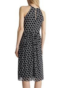 Robe sans manches en noir et blanc avec un motif et une taille froncée. Comprend une ouverture en forme de goutte dans le dos et une silhouette fluide.