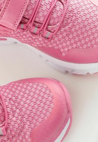 Des chaussures de course roses présentent un dessus en tissu texturé avec un motif tissé, des lacets élastiques et des semelles en caoutchouc lisses avec des accents.