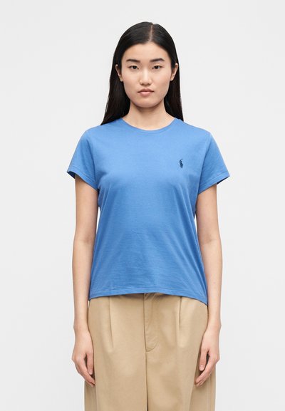 Kék pamut rövid ujjú póló kerek nyakkivágással és egy kis fekete logóval a bal mellrészen. Simogatott textúra és laza szabás.