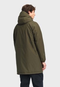 Manteau rembourré long, vert olive, avec capuche, doté de poignets élastiques et d'un cordon de serrage à l'ourlet. Texture de tissu lisse et imperméable.