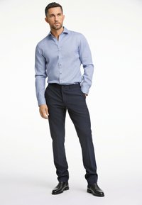 Lichtblauw overhemd met kleine witte patronen, gecombineerd met donkerblauwe pantalon en zwarte leren schoenen. Tailored fit en een zachte textuur.
