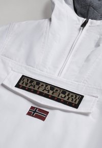 Anorak blanc avec une doublure grise, arborant un patch logo noir très visible et une petite broderie du drapeau norvégien en rouge. Fermeture éclair.