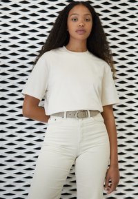 T-shirt en coton beige à manches courtes, associé à un pantalon en velours côtelé texturé gris clair et à une ceinture assortie avec une boucle circulaire.
