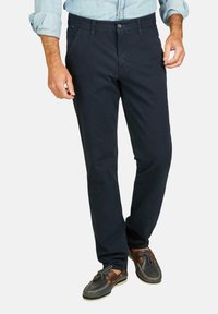 Marineblaue Baumwollchinos mit geradem Bein, seitlichen Taschen und einem Knopfverschluss an der Taille, kombiniert mit braunen Schuhen.