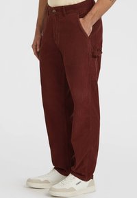 Bordeaux corduroy broek met wijde pijpen, voorzien van zijzakken en een knopen sluiting. Gepaard met witte sneakers en een neutraal topje.