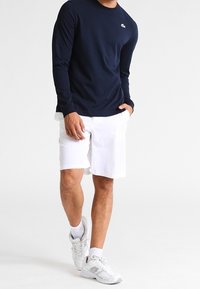 Camiseta de manga larga azul marino, logo en el pecho, pantalones cortos blancos, zapatos deportivos casuales, diseño limpio, tela suave, sin patrones ni detalles.