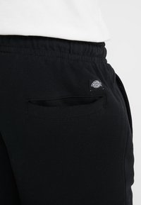 Černé tepláky vyrobené z bavlněné směsi, s elastickým pasem, bočními kapsami a malou nášivkou na zadní kapse.