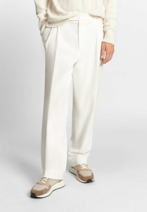 Un pantalon blanc à jambes larges avec une texture lisse et des plis à l'avant, associé à des baskets beiges et brunes avec des accents en maille et en daim.