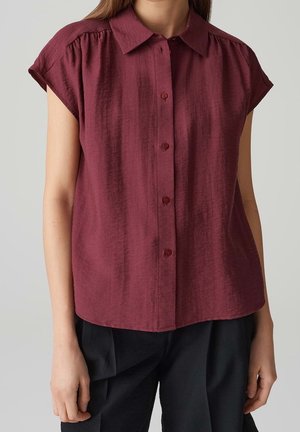 Burgundy short-sleeve shirt with a button-up front, textured fabric, and a classic collar. Features gathered stitching at the shoulders.