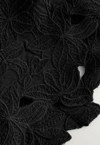 Tissu noir avec une broderie florale complexe et des feuilles texturées, mettant en valeur des points surélevés et des bords festonnés pour plus de détail.