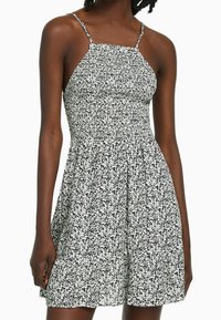 Black and white floral dress with a fitted bodice, thin straps, and a flared skirt, made of lightweight fabric with a textured pattern.