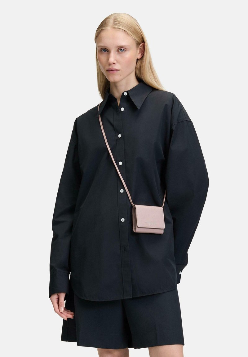 Schwarze, übergroße Button-Up-Bluse mit langen Ärmeln, kombiniert mit einem dunklen Rock. Eine kleine rosa Umhängetasche setzt einen Kontrast.