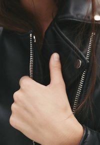 Chaqueta de cuero negro con cremallera plateada. Primer plano de una mano agarrando el cuello, resaltando la textura suave y el diseño elegante.