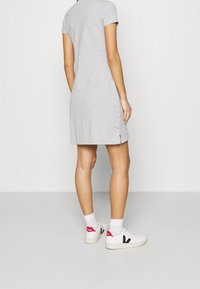 Grijze katoenen jurk met korte mouwen, knie-lang, met zijsplitten. Gecombineerd met witte sneakers met rode en zwarte accenten.