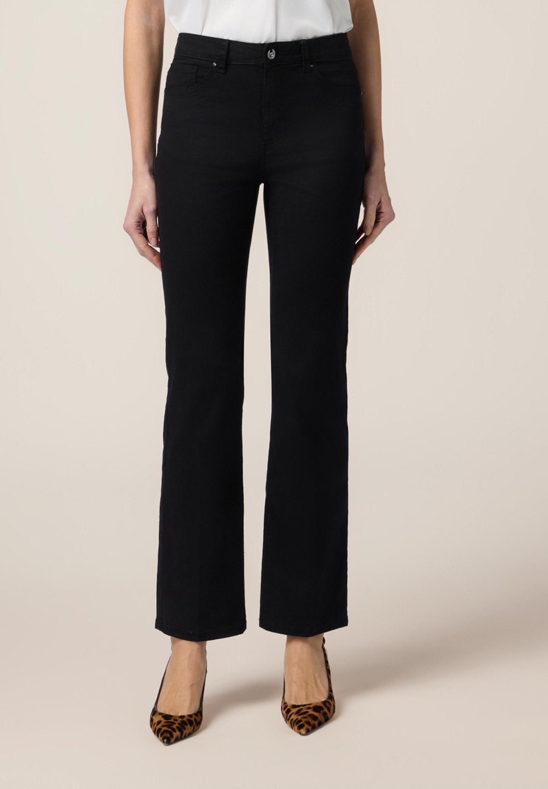 Zwarte flared jeans van denim met een gladde textuur. Voorzien van een knoop aan de voorkant, riemlussen en zijzakken. Draagt met gemusterde hakken.