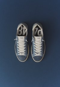Paire de baskets bleu et blanc à lacets avec "P448" sur la languette, reposant sur une surface bleu foncé, vue d’en haut.