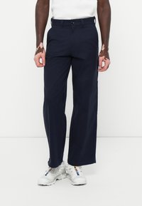 Calças largas azul-marinho feitas de tecido leve. Apresenta um fecho de botão na frente e bolsos laterais. Combinadas com sapatilhas brancas.