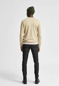 Pullover beige in maglia, jeans in denim scuro e un berretto verde in maglia. Il pullover ha maniche lunghe e scollatura rotonda. Texture liscia.