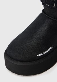 Botín negro de tobillo hecho de material suave, con una suela negra gruesa y una parte superior texturizada, con un detalle del logo "KARL LAGERFELD" en blanco.