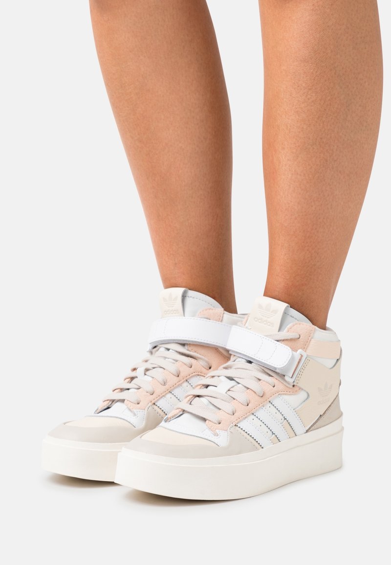 Höga skor i vitt och ljusrosa, med en kombination av läder och mocka, snörning framtill och justerbart rem för stöd.