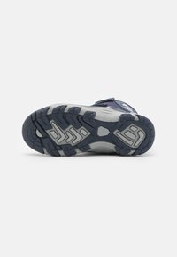 Chaussure de sport bleue avec une semelle en caoutchouc robuste. Elle est dotée de deux sangles Velcro ajustables et d'accents gris texturés sur la semelle extérieure.