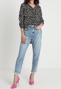 Hedvábná blůza s černobílým vzorem a límečkem, kombinována se světle modrými džíny s roztrhanými okraji a růžovými vysokými podpatky.