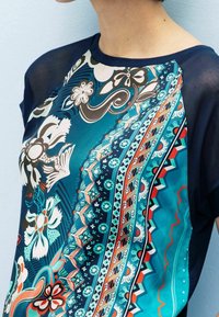 Short-sleeve top featuring a vibrant blue and green floral pattern, contrasting dark navy sleeves, and a smooth, lightweight fabric.
