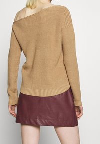 Beige, schulterfreier Strickpullover mit langen Ärmeln und geripptem Muster, kombiniert mit einem burgunderroten Leder-Minirock mit glatter Oberfläche.