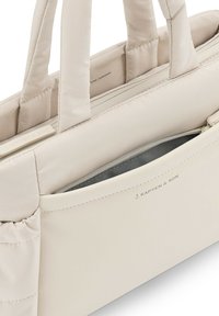 Vaaleanbeige pehmustettu olkalaukku, jossa on kaksinkertaiset lyhyet kahvat, varustettuna vetoketjullisella taskulla ja huomaamattomalla brändäyksellä ulkopuolella. Sujuva, pehmeä tekstuuri.