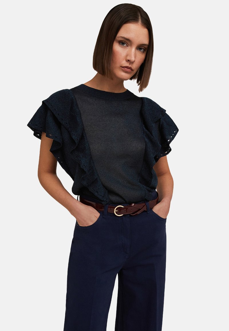 Granatowa bluzka z falbaniastymi rękawami, wykonana z dzianiny; zestawiona z granatowymi spodniami o wysokim stanie i brązowym paskiem z złotą klamrą.