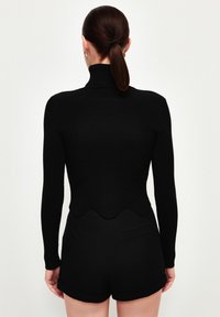 Schwarzes geripptes Rollkragenoberteil mit gewelltem Saum, kombiniert mit schwarzen Shorts mit elegantem Design und umgeschlagenen Kanten.
