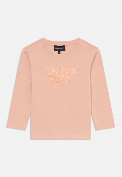 Gaiši rozā krāsas bērnu krekls ar garām piedurknēm, apaļu apkakli un teksturētu spīdīgu ērģeļa logotipu krūtīs.