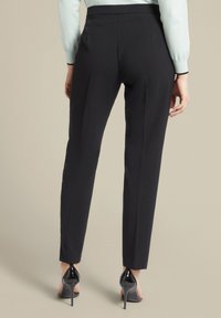 Zwarte op maat gemaakte broeken met een slank model, met een gladde textuur en een hoge taille. Gecombineerd met gepatineerde zwarte high-heel schoenen.