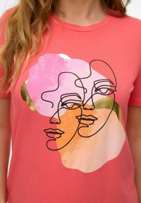 Korale t-shirt z czarnym rysunkiem dwóch abstrakcyjnych twarzy na tle kolorowych kształtów w odcieniach różu, pomarańczy i złota.