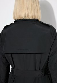 Czarny płaszcz trench z paskiem w talii, z tylnym klapą i detalami guzika. Gładka tekstura i czyste linie tworzą wyraźną sylwetkę.