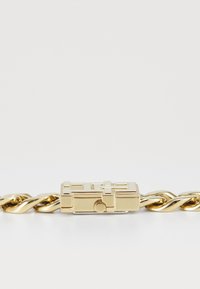 Bracciale in metallo dorato con un design a catena attorcigliata, dotato di una chiusura quadrata e dettagli geometrici sulla superficie della chiusura.