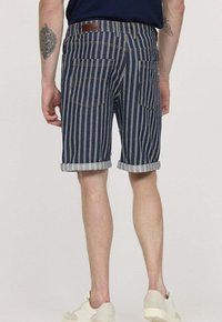 Shorts en denim rayés navy avec ourlets retroussés, dotés de deux poches arrière et d'une étiquette en cuir sur la ceinture. Texture lisse.